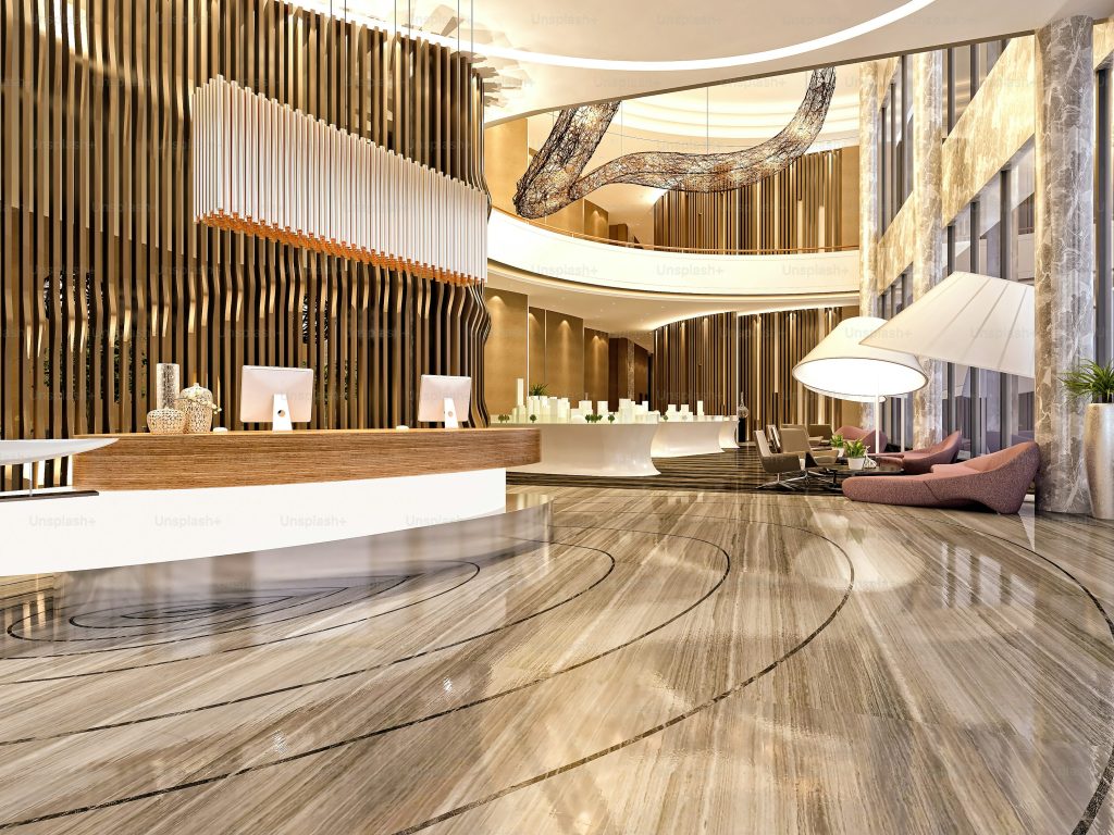 Contemporary hotel lobby with elegant reception desk, artistic lighting fixtures, and stylish seating area featuring marble floors and tall windows.