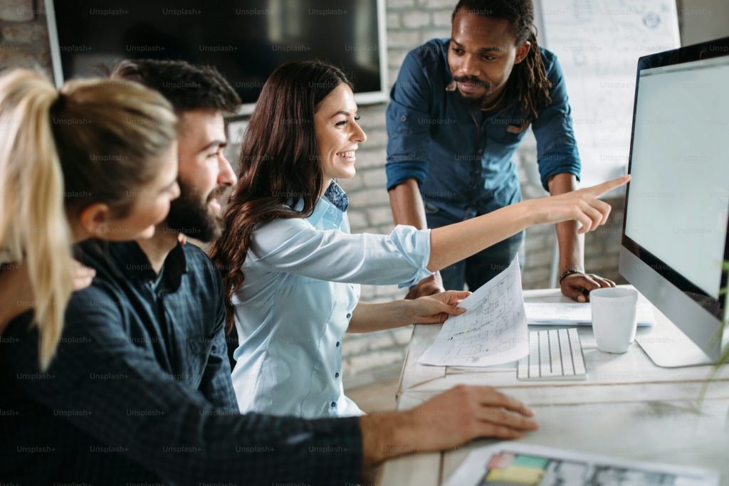 Group of professionals collaborating in office, woman leading team discussion by pointing at computer screen during business meeting
